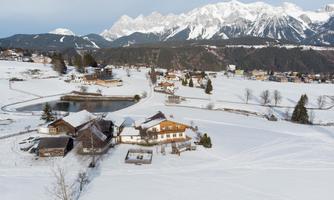 A snowy landscape with quiet houses and a small pond. In the background, majestic mountains can be seen.