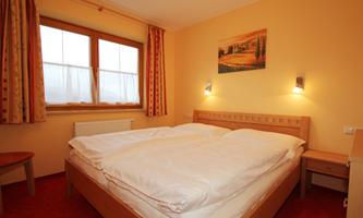 A cozy bedroom with a large double bed and a bright window. The walls are painted in warm colors and there is a beautiful picture on the wall.
