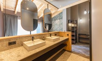 A modern bathroom with two sinks and large round mirrors. The walls are elegantly designed and there is plenty of natural light.