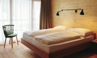 A modern bedroom with a large double bed and wooden paneling. A cozy chair is placed next to the window with curtains.