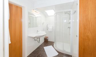 A modern bathroom with a shower, sink, and a large mirror. The walls are light and the floor is dark, creating a nice contrast.