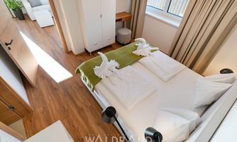 A modern bedroom with a double bed and wooden floor. There are decorative towels shaped like swans and a bright, inviting atmosphere.