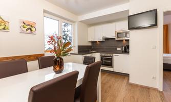 A modern kitchen unit with a dining table and chairs. The room is bright and friendly, with decorative pictures and a flower on the table.