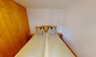 A cozy bedroom with a double bed and two pillows. The walls are bright and a wooden shelf complements the modern design.