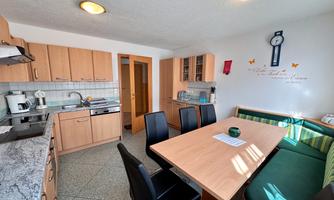 A modern kitchen with wooden cabinets and a dining area. The room is bright and friendly, equipped with modern appliances.