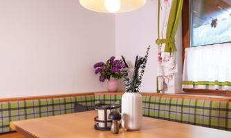A cozy dining area with a wooden table and a bench. A vase with flowers and a candle is on the table.