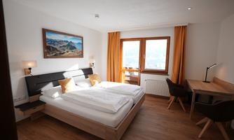 A modern bedroom with a large double bed and wooden-colored floor. Through the window, you can see the mountains, and the room is bright and cheerfully decorated.