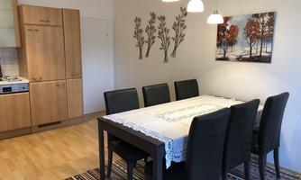A cozy dining area with a large table and six chairs. The walls are decorated with a picture and decorative elements.