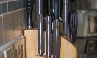 A knife block made of wood with various kitchen cutting tools. The knives have black handles and are neatly stored.