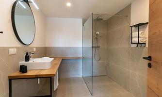 A modern bathroom with a clear shower cabin and an elegant sink. The walls are designed in bright, neutral tones.