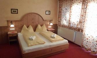 A cozy bedroom with a double bed and two pillows. The walls are painted in soft colors and the windows have curtains with a colorful pattern.