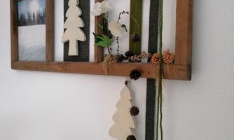 A decorative wall design made of wood with Christmas tree ornaments and natural materials. There are also images with winter motifs and a green cord.