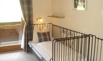 A cozy room with an iron bed and soft pillows. A window with curtains provides daylight.