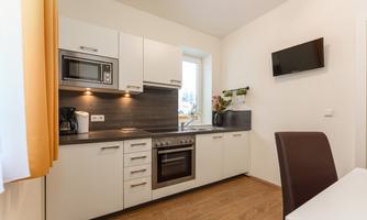 A modern kitchen with white cabinets and wooden floors. Equipped with a stove, microwave, and a small table.