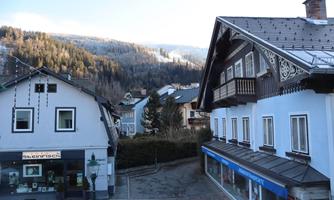 A picturesque street in a small village with traditional houses. In the background, wooded mountains can be seen.