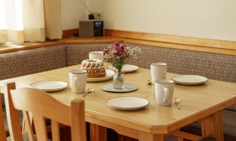 A cozy dining table with white dishes and cups. In the center is a flower vase and a cake on a plate.