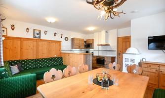 A cozy kitchen with wooden cabinets and a large dining table. The walls are equipped with traditional decorations and a television.