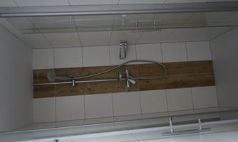 A modern shower with glass doors and a wooden panel in the middle. The walls are tiled and appear bright and clean.