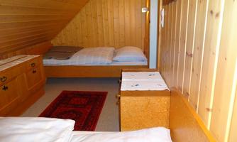 A cozy room with wooden paneling and two single beds. A red carpet gives the room a warm atmosphere.