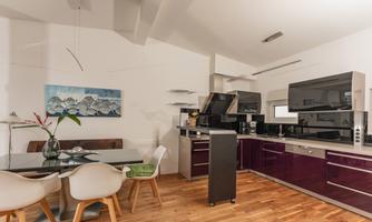 A modern kitchen with purple cabinets and sleek appliances. Next to the kitchen is a dining area with a table and chairs.