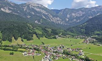 A picturesque mountain landscape with a small village in a green valley. The surrounding mountains and the blue sky give the scene a peaceful atmosphere.