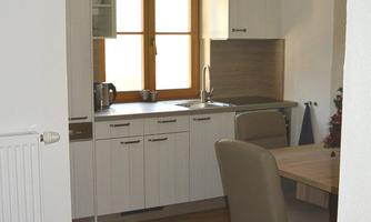A modern kitchen with bright furniture and a dining area. Large windows provide plenty of daylight in the friendly room.
