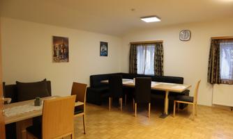 A cozy dining area with wooden tables and chairs. Windows with curtains provide natural light.