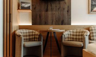 A cozy room with two upholstered chairs and a small table. A television is mounted on the wall, and wooden paneling provides a warm ambiance.
