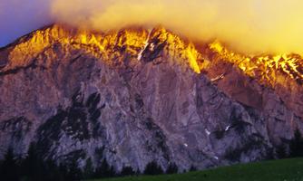 A majestic mountain with glowing rocks at sunset. Clouds frame the peaks and give the scene an impressive atmosphere.