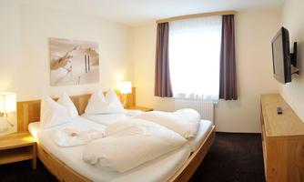 A cozy hotel room with a double bed and white bedding. The room is bright and modernly furnished, with a window and a television.