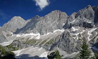 An impressive mountain landscape with tall, gray rocks and snow-capped peaks. The sky is clear and blue, creating a beautiful backdrop.
