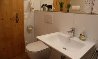 A modern bathroom with a white sink and toilet.  
Wooden panels and plants create a cozy atmosphere.