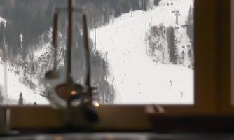 A snowy mountain landscape is visible through a window. In the foreground, glasses and cutlery are placed on a table.