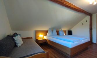 A cozy bedroom with a double bed and a sofa bed. The sloped ceiling and wooden details give the room an inviting atmosphere.