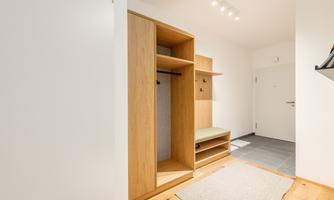 A modern entrance area with a wooden cabinet and a bench. The floor is tiled with gray tiles and there is a carpet.
