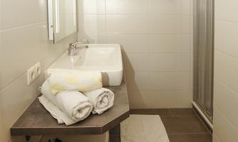 A modern bathroom with a shower and a sink. Towels and a hairdryer are neatly stacked on a table.