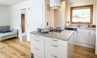 A modern kitchen with a central kitchen island and white cabinets. The room is bright and inviting, with a cozy sofa in the background.