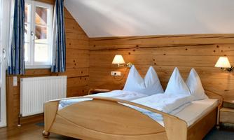 A cozy bedroom with wooden paneling and two beds. The walls are light, and there are windows with blue curtains.