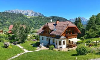 A beautiful house in the midst of a picturesque landscape. Mountains and plenty of greenery surround the building.