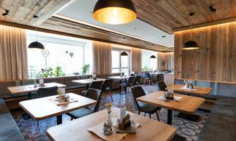 A modern restaurant with wooden furniture and warm lighting. The tables are beautifully decorated and offer an inviting atmosphere.