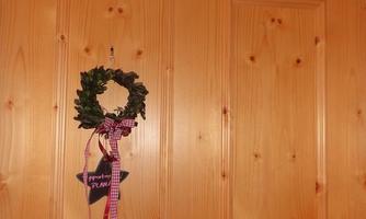 A wooden door with a green wreath decoration and a purple bow. Above is an oval plaque with a fine embellishment.