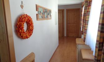 A bright hallway with wooden paneling and an orange garland decoration on the wall. On the left side, there are dressers and colorful curtains at the windows.