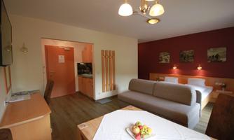 A cozy living room with a gray sofa and a table with fruits on it. The walls are painted in soft colors, and there is gentle lighting.
