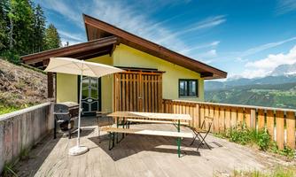 A cozy holiday home with a terrace and an outdoor dining table. In the background, green hills and mountains can be seen.