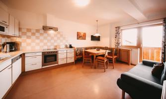 A modern kitchen with a dining table and a cozy living room. Large windows provide plenty of natural light.
