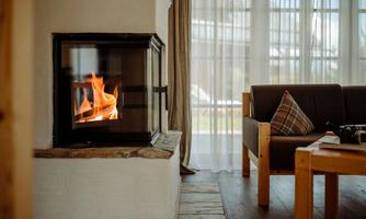 A cozy room with a modern fireplace that displays a warm fire. Next to it is an inviting sofa with cushions.