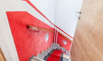 A bright staircase with red walls and wooden details. The steps are modern and invite you to go down.