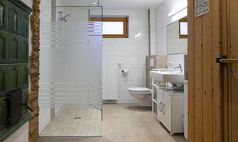 A modern bathroom with a glass shower and white sink. The walls are light tiled and there are wooden details.
