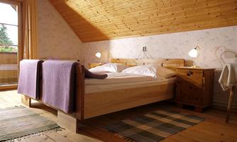 A cozy bedroom with a wooden ceiling and a large bed. Next to the bed is a bedside table and there is a nice view outside.