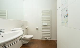 A modern bathroom with a sink, a toilet, and a towel rack. The walls are bright and the floor is made of dark material.